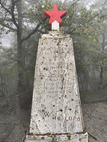 Monumento dedicato ai caduti di Monte Sole, con una stella rossa, immerso nella nebbia e circondato da alberi.