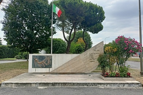Il Monumento alla libertà, con bandiera italiana, circondato da alberi e fiori. Un omaggio significativo.