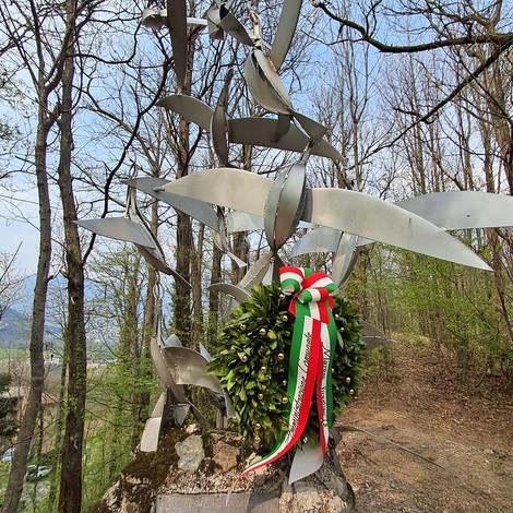 Monumento a Volpato con foglie metalliche e corona d'alloro, immerso nel verde. Atmosfera commemorativa.