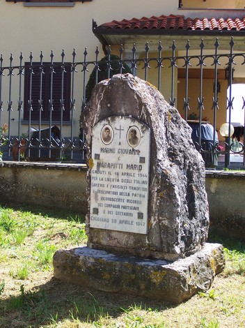 Cippo commemorativo in marmo dedicato a Mario Marapitti, situato in un'area verde e affacciato su una recinzione.