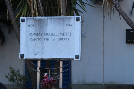 Lapide commemorativa a Romeo Guglielmetti, caduto per la libertà, con dettagli storici e decorazioni floreali.