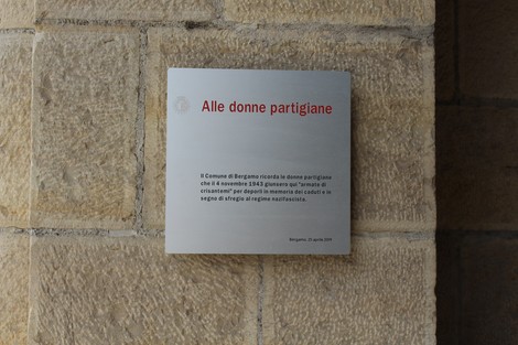 Targa commemorativa dedicata alle donne partigiane, situata su un muro di pietra a Bergamo.
