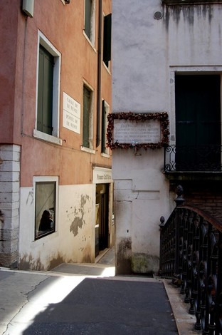Vicolo caratteristico di Venezia con la lapide a Perini, circondata da edifici storici e una suggestiva luce.