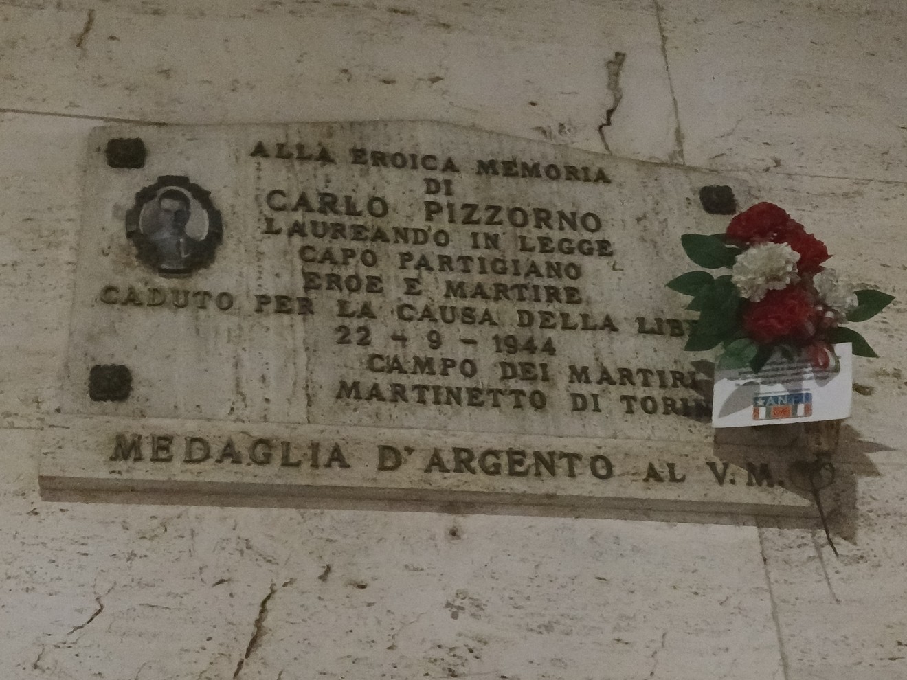 Lapide commemorativa a Carlo Pizzorno, partigiano caduto per la libertà nel 1944, con decorazioni floreali.