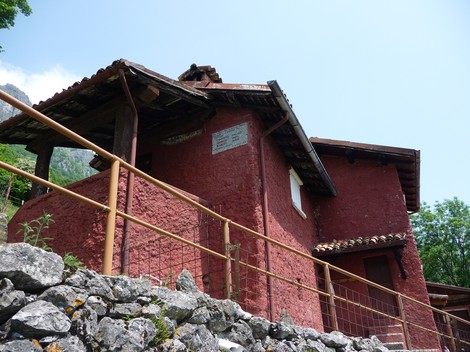 Lapide commemorativa su una costruzione in pietra, situata in un contesto naturale montano.