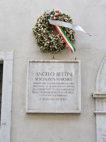 Lapide commemorativa di Angelo Bettini, socialista martire, adornata da una corona di fiori e nastri tricolore.