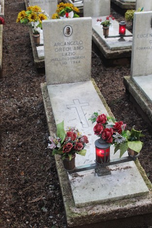 Tombe affiancate con fiori freschi e candele, dedicate ai caduti per la Libertà. Atmosfera di rispetto e commemorazione.