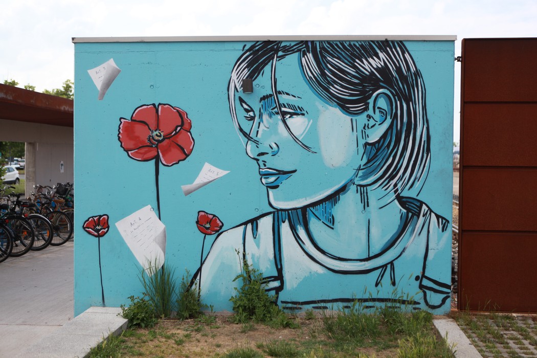 Murale che ritrae una giovane donna con papaveri rossi, su uno sfondo azzurro. Arte urbana evocativa e colorata.