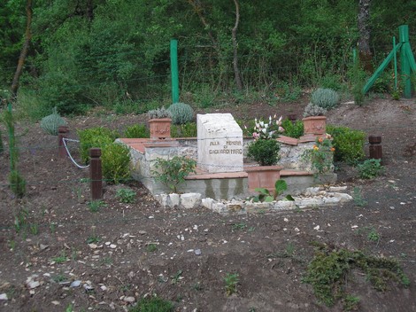 Cippo commemorativo in un'area verde, adornato con piante e fiori, a Gagliardi.
