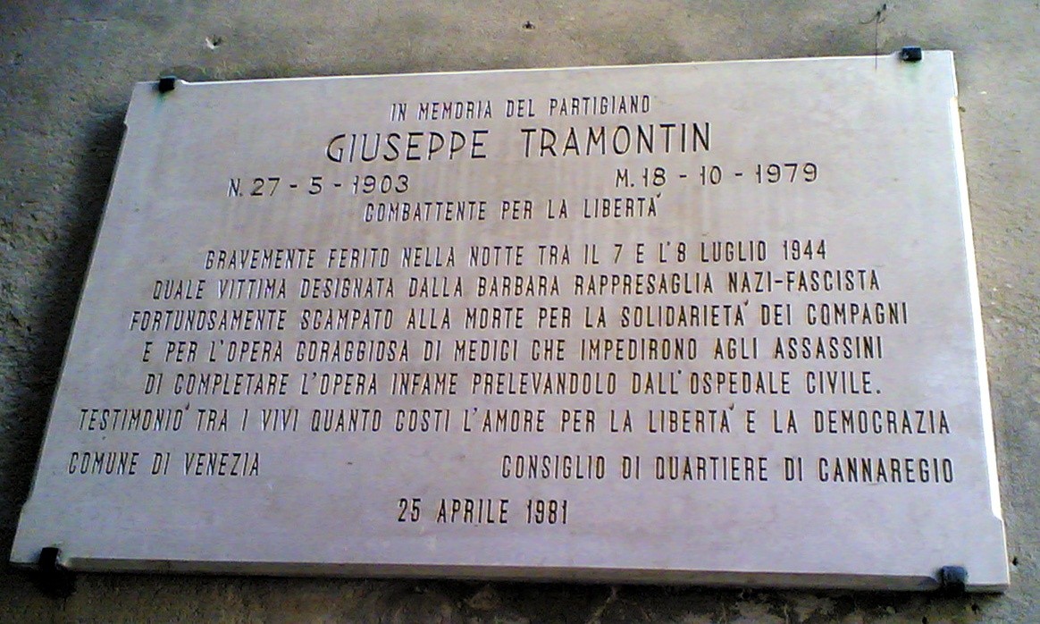 Lapide commemorativa dedicata a Giuseppe Tramontin, partigiano, con iscrizioni su un fondo chiaro.