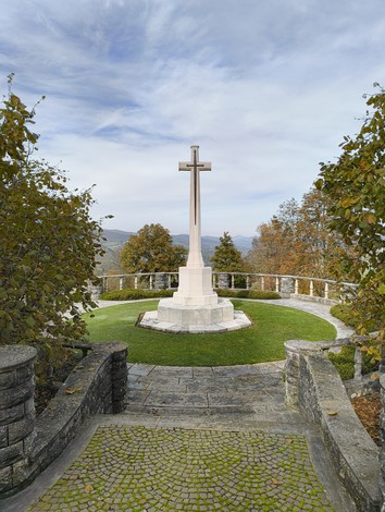 Cimitero di guerra sudafricano con croce centrale e panoramica circondata da alberi e colline.