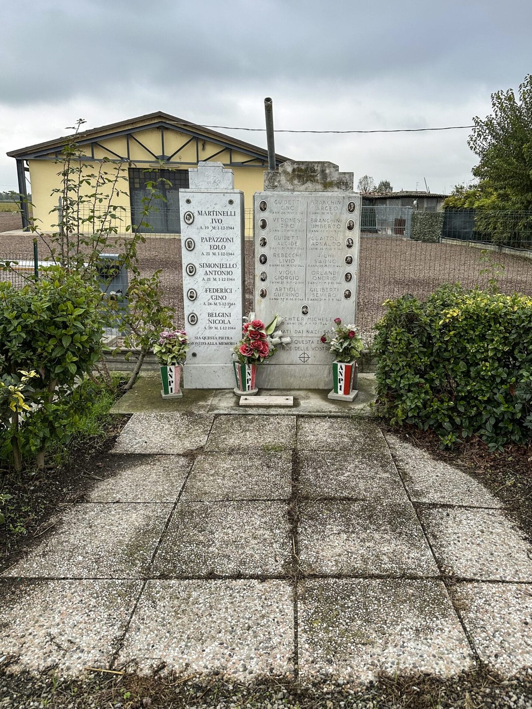Monumento ai caduti partigiani di Cortile, con iscrizioni e fiori commemorativi.