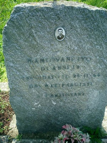 Cippo funerario di Mantovani, con foto nel rilievo e iscrizioni su pietra, immerso nel verde circostante.