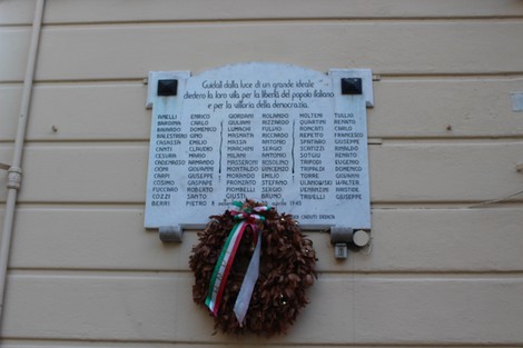 Lapide commemorativa dedicata ai caduti per la libertà, con nomi incisi e corona di fiori decorata.