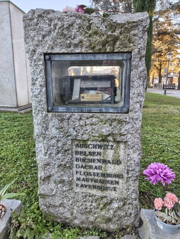 Cippo commemorativo dedicato ai caduti nei lager, con iscrizioni e decorazioni floreali.