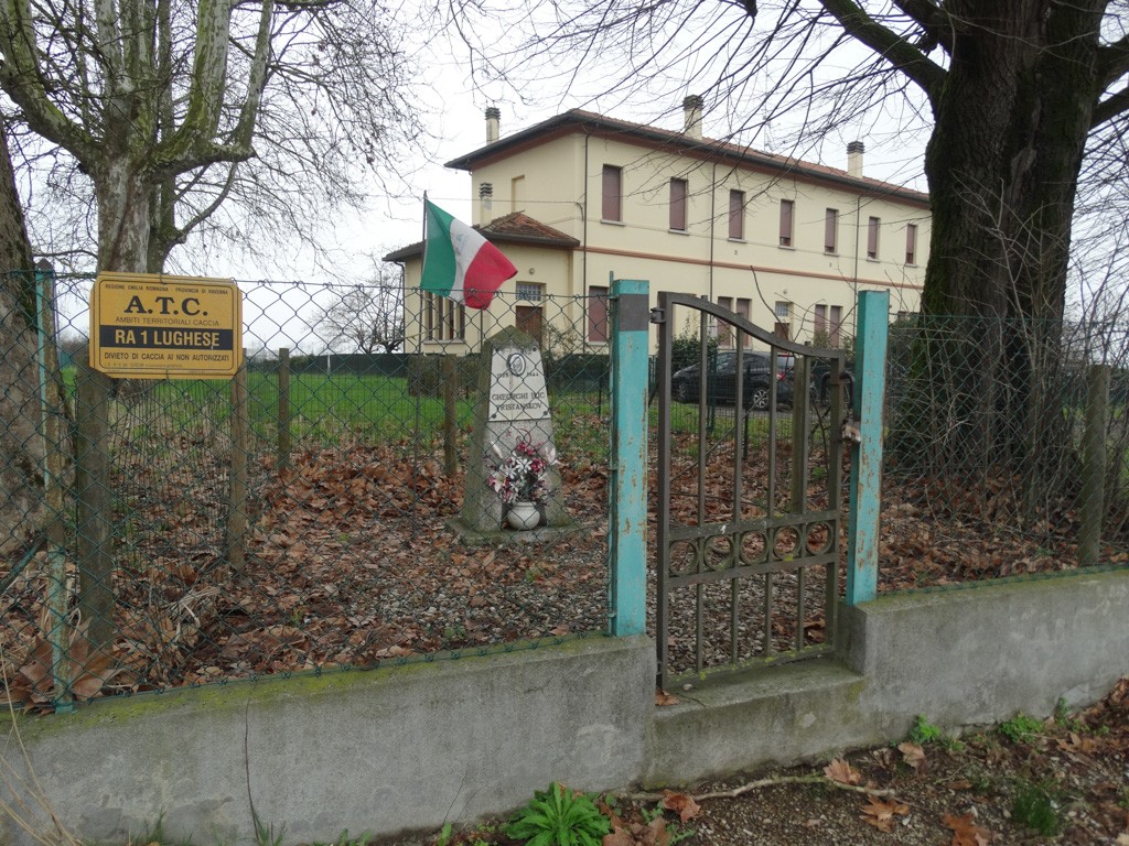 Cippo commemorativo a Pristanskov, circondato da un recinto e alberi, con bandiera italiana.