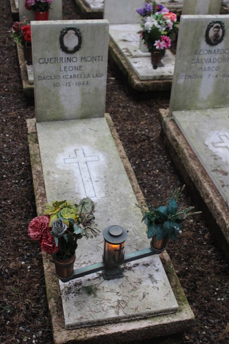 Tombe decorate con fiori in memoria dei caduti per la Libertà, con croce e lumino attivo.