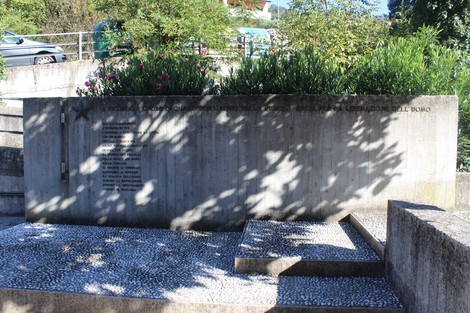 Monumento alla Resistenza con struttura in cemento e fiori, immerso nel verde, dedicato alla memoria storica.