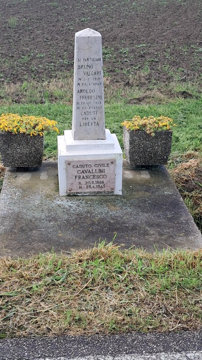 Cippo commemorativo dedicato a Vaccari, Tredesini e Cavallini, con aiuole di fiori gialli circostanti.