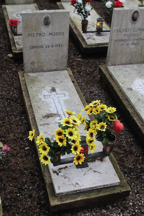 Tombe bianche adornate con fiori gialli, dedicate ai caduti per la Libertà. Atmosfera di rispetto e memoria.