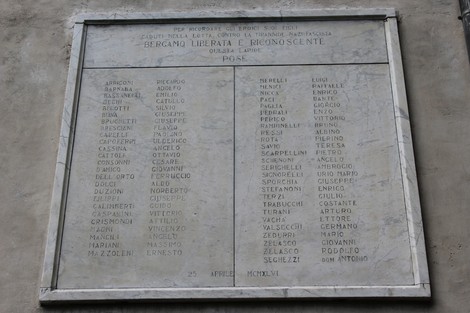 Stele commemorativa dedicata ai partigiani caduti, con nomi incisi in marmo su fondo chiaro.