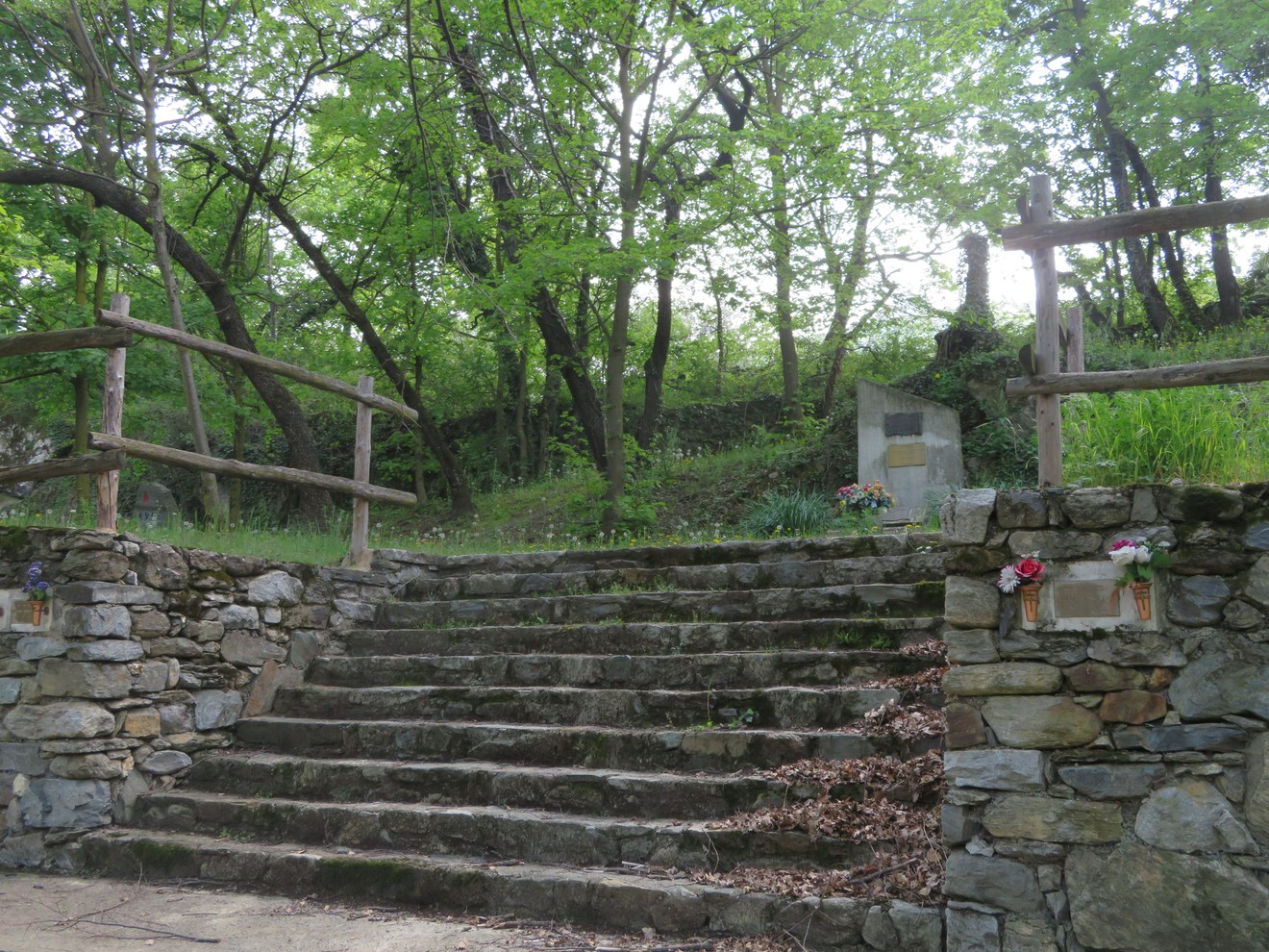 Monumento nel Parco della Rimembranza, immerso nel verde, con scale di pietra e decorazioni floreali.