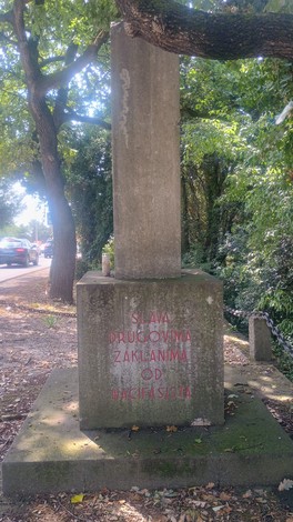 Monumento commemorativo con iscrizione, circondato da alberi e strada, in ricordo dei caduti per rappresaglia.