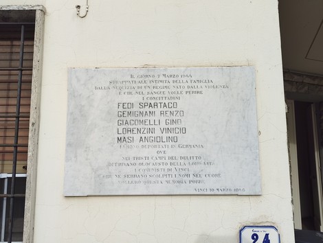 Lapide commemorativa ai deportati, con nomi e date, posta su una parete esterna. Rappresenta la memoria storica.