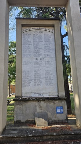 Monumento ai caduti con nomi incisi in memoria delle guerre, circondato da alberi e spaziosa area verde.