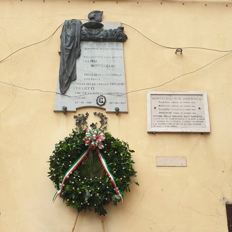 Lapide commemorativa in onore delle vittime civili, con corona di fiori, su un muro di monumento storico.