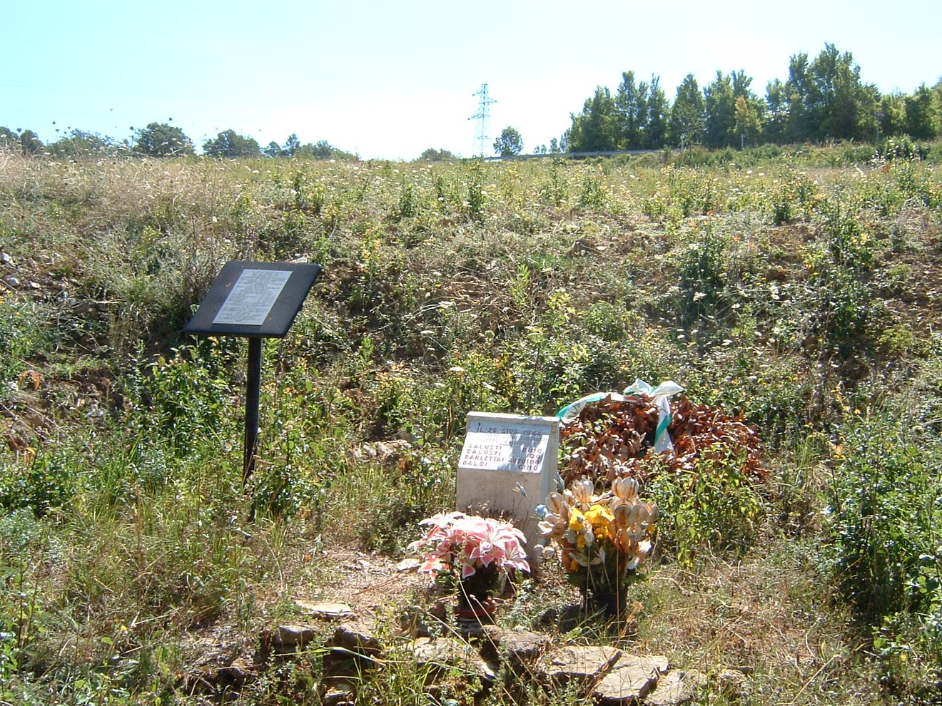 Cippo commemorativo dedicato ai partigiani di Gerfalco, circondato da natura e fiori.