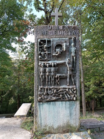 Memoriale dedicato ai caduti della Benedicta, con rilievi artistici su pietra tra vegetazione.