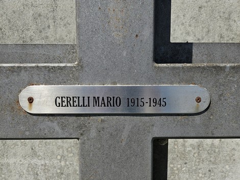 Croce commemorativa in metallo con una targa che riporta nome e date di nascita e morte.