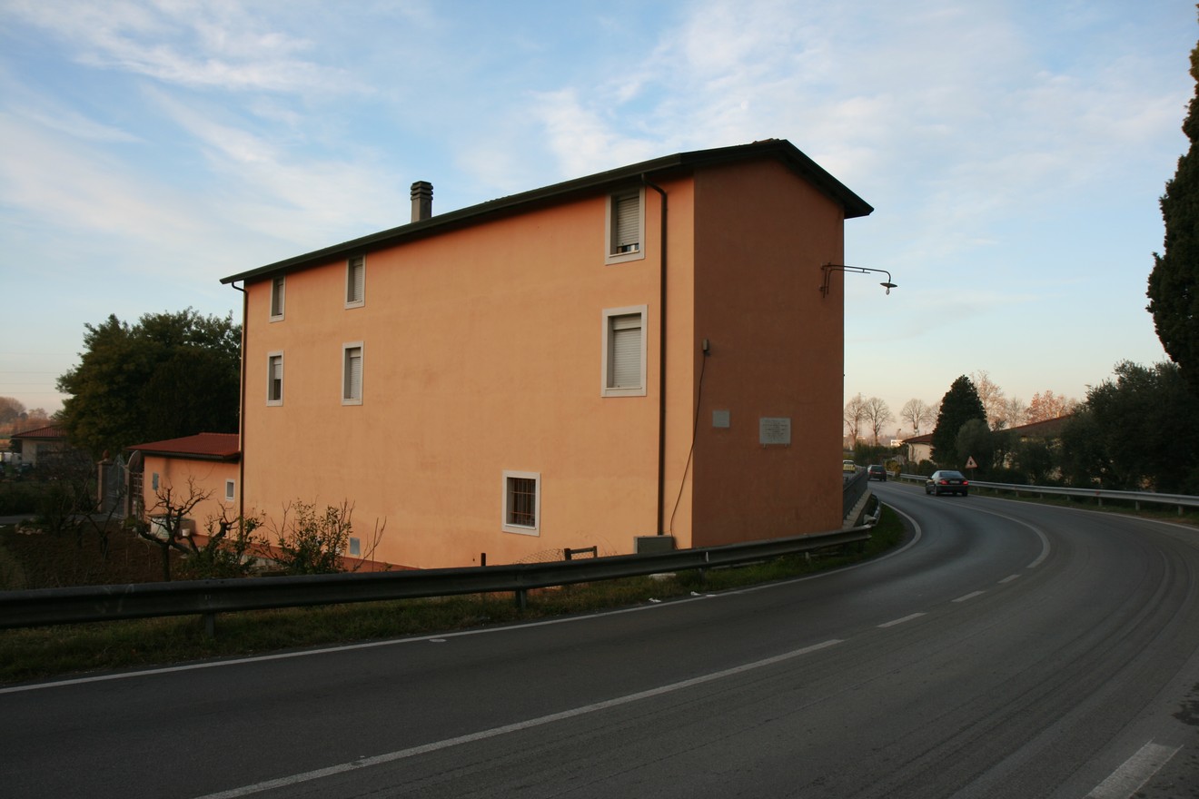 Lapide di Sassaia, edificio lungo strada con muratura arancione e vegetazione circostante.