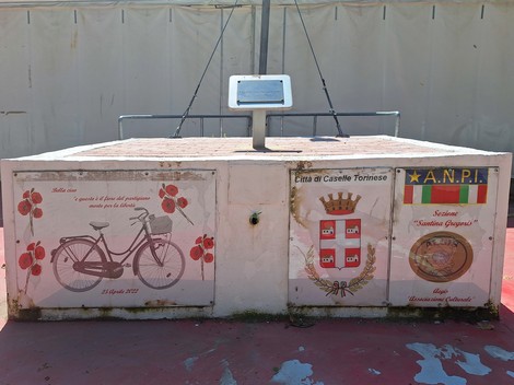 Targa decorativa a Noce con simboli locali e un'immagine di bicicletta in un contesto urbano.