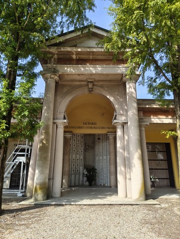 Ingresso del Sacrario dei caduti, con architettura classica e ornamenti, circondato da alberi verdi.