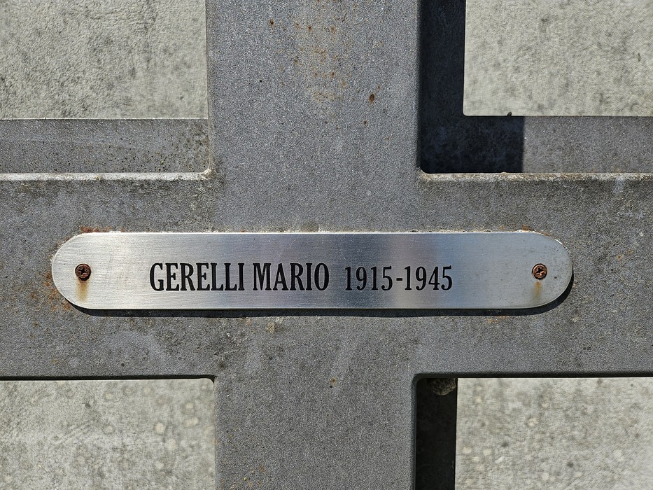Croce commemorativa in metallo con una targa che riporta nome e date di nascita e morte.