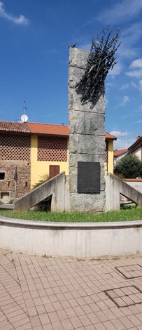 Monumento ai combattenti per la Libertà, con una struttura in pietra e un elemento decorativo in ferro, circondato da verde.