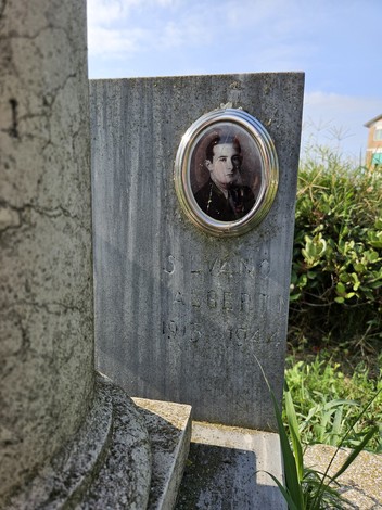 Cippo funerario con fotografia di Silvano Alberti, circondato da vegetazione e sotto un cielo sereno.