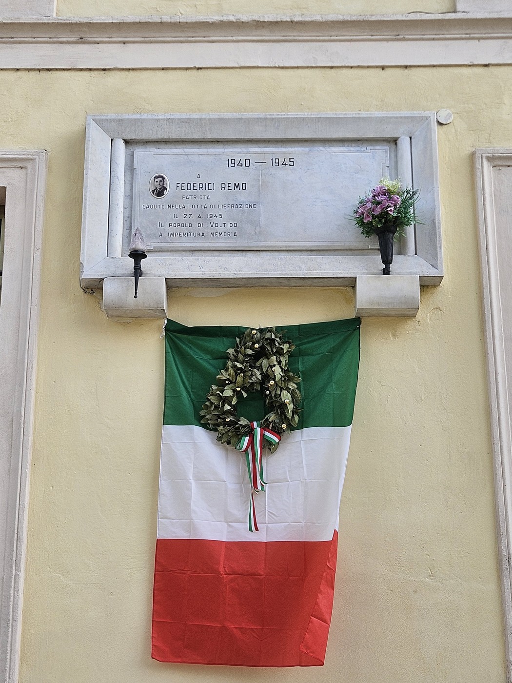 Lapide commemorativa dedicata a Federici, decorata con un drappo tricolore italiano e fiori.