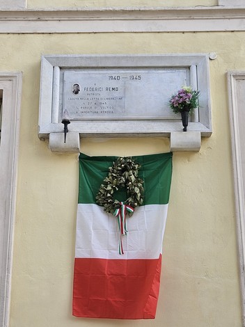 Lapide commemorativa dedicata a Federici, decorata con un drappo tricolore italiano e fiori.