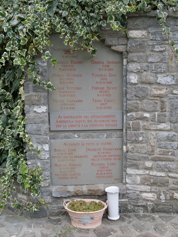 Lapide commemorativa dedicata ai caduti del Distaccamento Amendola, decorata con edera, in un contesto storico.