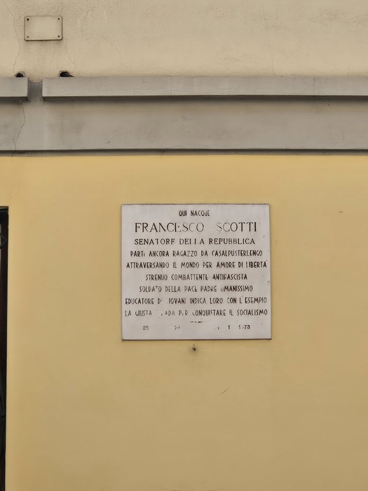 Lapide commemorativa di Francesco Scotti, senatore della repubblica, su muro giallo.