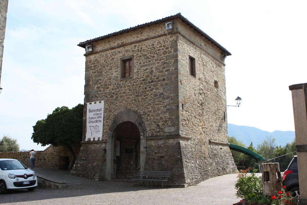 Lapide ai caduti di Cascio, monumento in pietra con torre storica, circondato da un'area verde e fiorita.