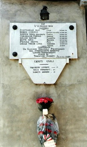 Lapide commemorativa ai caduti partigiani, con nomi e omaggio floreale, in ricordo della Resistenza.