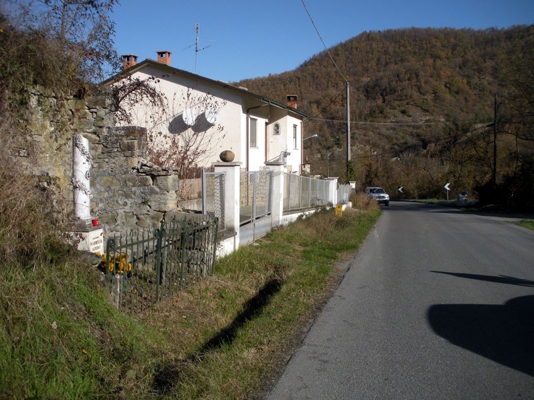 Vista di un cippo a Pochintesta, con caratteristico paesaggio collinare e abitazioni lungo la strada.