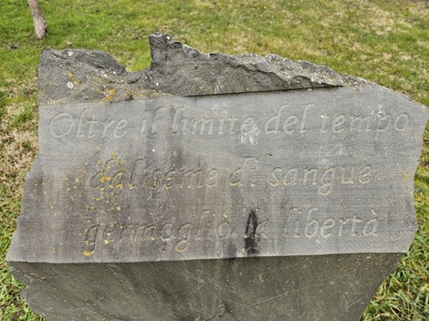 Monumento ai Partigiani con iscrizione commemorativa su una pietra, immerso nel verde circostante.