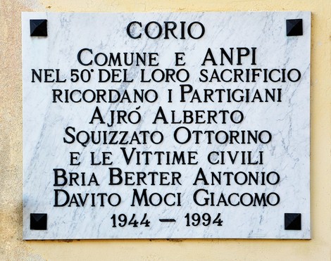 Lapide in marmo bianco con cornice e angoli metallici, affissa su una parete, con iscrizione dedicatoria.
