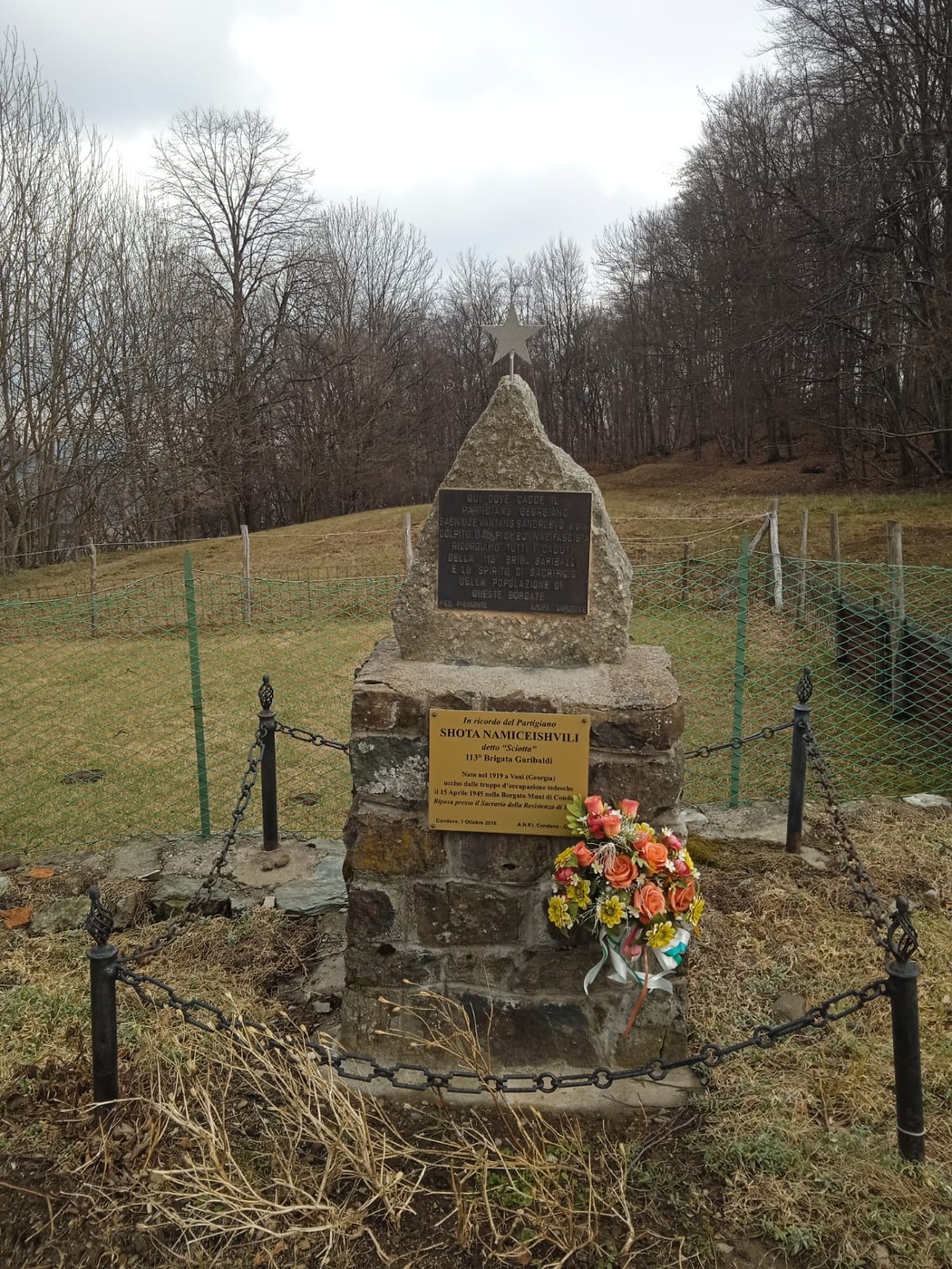 Cippo commemorativo a Namiceishvili, circondato da natura e fiori, in un'area tranquilla e storica.