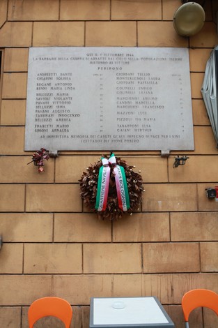 Lapide commemorativa dei bombardamenti del 1944, con elenchi di nomi e una corona di fiori decorativa.